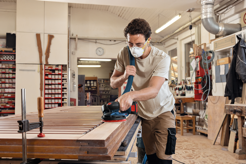 Image of worker using the Bosch GEX18V-150-3N 18V 6” Random Orbit Sander (3/32”) for finishing a wooden strips.