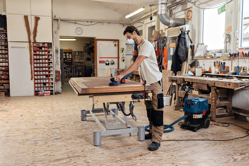 Image of worker using the Bosch GEX18V-150-3N 18V 6” Random Orbit Sander (3/32”) for finishing a wooden strips.