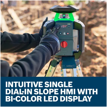 A worker in gloves adjusting the slope on a Bosch GRL18V-34K rotary laser level on a tripod at a construction site.