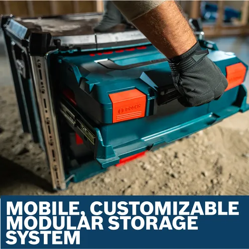 Worker wearing gloves lifts a blue and red Bosch RACK-2 L-BOXX Contractor Rack on a dusty construction site.