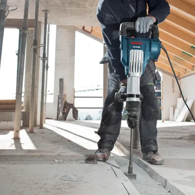 Person wearing safety gear using a rotary hammer to break concrete.