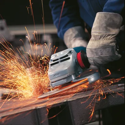 Person wearing protective gloves using a grinder, sparks flying.