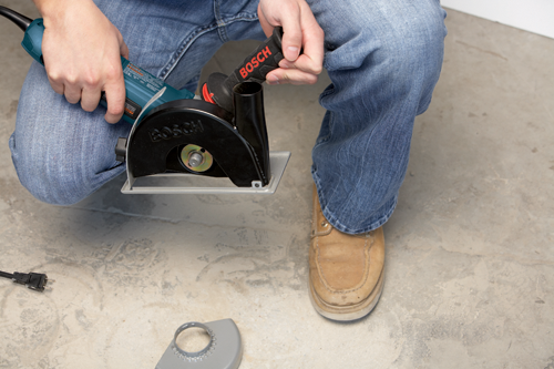 Person holding a Bosch power tool, wearing blue jeans and tan shoes.