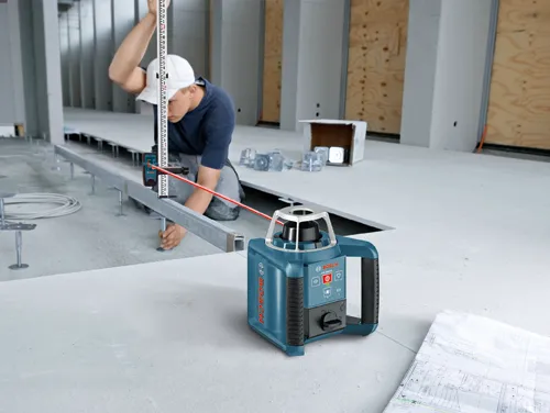 A person using a Bosch GRL300HV rotary laser level and a measuring stick for construction purposes.