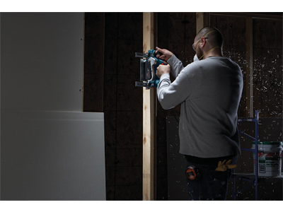 Persona que lleva equipo de protección utilizando una herramienta eléctrica para cortar una viga de madera.