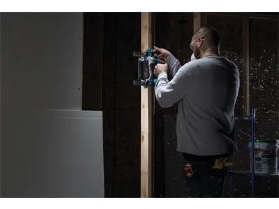 Persona que lleva equipo de protección utilizando una herramienta eléctrica para cortar una viga de madera.