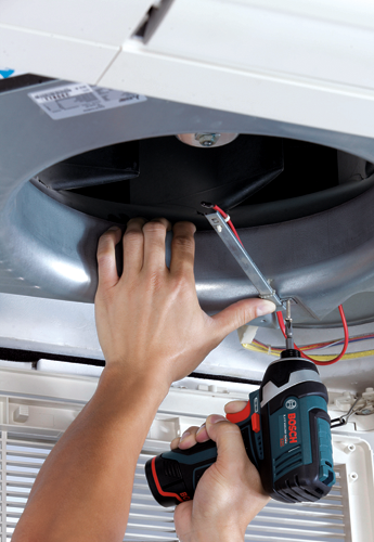 Una persona utiliza un atornillador de impacto Bosch de 12V con batería de iones de litio para instalar algo dentro de una unidad de ventilación de aire.