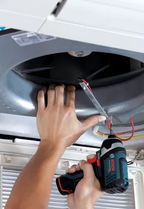 Una persona utiliza un atornillador de impacto Bosch de 12V con batería de iones de litio para instalar algo dentro de una unidad de ventilación de aire.