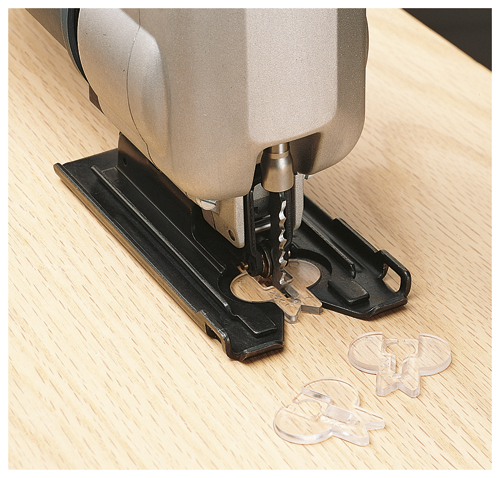 Una sierra de calar cortando piezas de plástico transparente sobre una superficie de madera.