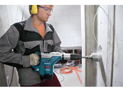 Persona que lleva gafas de protección y protección auditiva taladrando una pared de hormigón con un martillo Bosch, modelo 1125EVS.