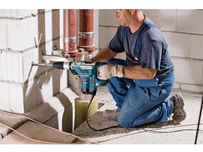 Persona arrodillada, con guantes, utilizando una herramienta eléctrica Bosch para taladrar una pared.