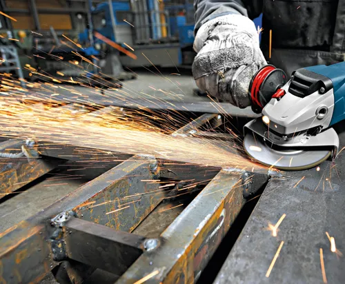 Persona utilizando una amoladora en metal, generando chispas.