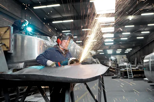 Bosch LBM 18-125 S amoladora en uso por una persona que lleva equipo de protección, con chispas volando.