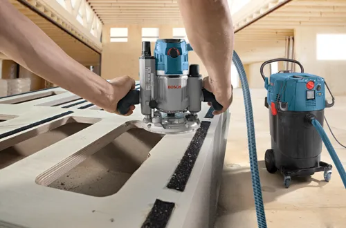 Fresadora Bosch cortando madera, sistema de aspiración de polvo en segundo plano.