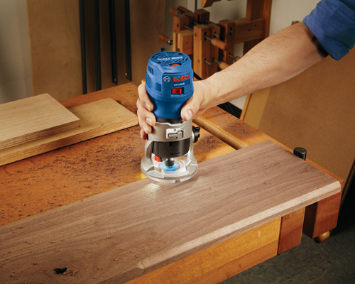 Bosch GKF125CE Colt, fresadora de 1,25 HP, siendo utilizada sobre una tabla de madera por una persona.