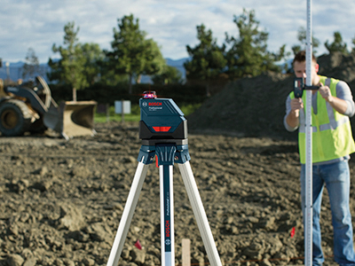 Nivel láser Bosch Professional sobre trípode, con una persona con chaleco de seguridad utilizando una mira telescópica.
