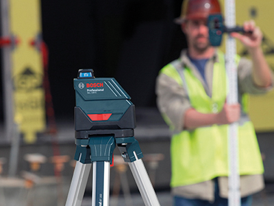 Nivel láser Bosch Professional GCL 2-15, con una persona que lleva un casco y un chaleco de alta visibilidad en el fondo.