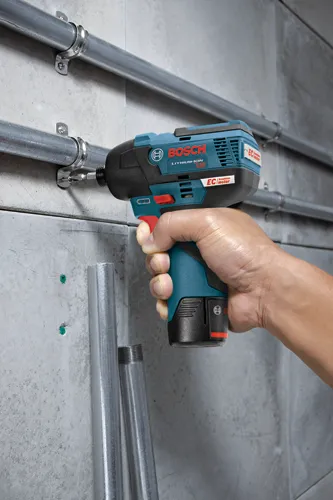 Bosch ATORNILLADOR DE IMPACTO con motor EC sin escobillas de 12 V de IONES DE LITIO, sostenido con la mano, atornillando un tornillo en un soporte fijado a una tubería metálica en una pared de hormigón.