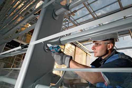 Hombre con gafas de seguridad y casco utilizando un taladro con motor EC Bosch para trabajar en una estructura metálica.