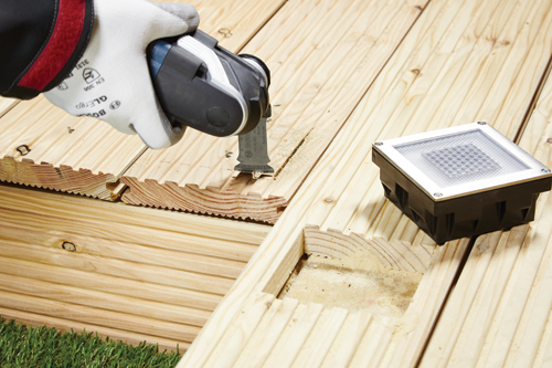 Hoja de sierra curva Bosch AIZ 32 EPC HC Swiss Made cortando una tarima de madera, con una luminaria cerca.