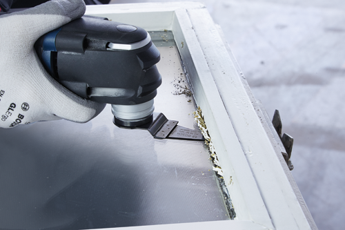 Herramienta multiusos Bosch con hoja A12 28 SC HCS Multi Material retirando material de un marco de ventana.