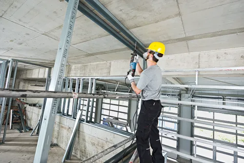 Trabajador de la construcción con casco y equipo de seguridad, taladrando un techo.