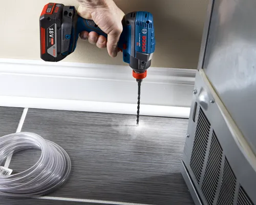 Taladro Bosch 18V de iones de litio en uso, perforando un agujero en el suelo, con un rollo de tubos transparentes a la izquierda.