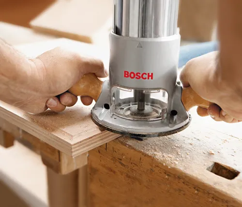 Fresadora Bosch siendo utilizada en una tabla de madera, aserrín visible, 'BOSCH' impreso en la herramienta.