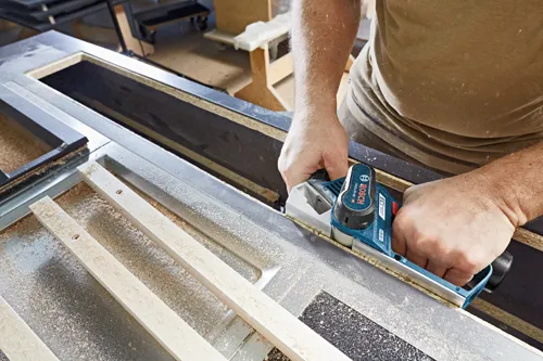 Cepillo profesional Bosch GHO 12V-20, con manos de una persona trabajando en madera.