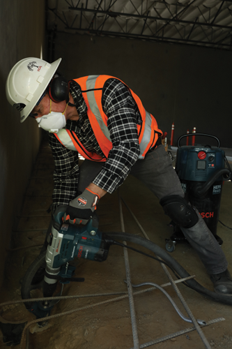 Persona que lleva equipo de protección operando un Boschhammer Bosch 11264EVS, aspiradora posicionada cerca.
