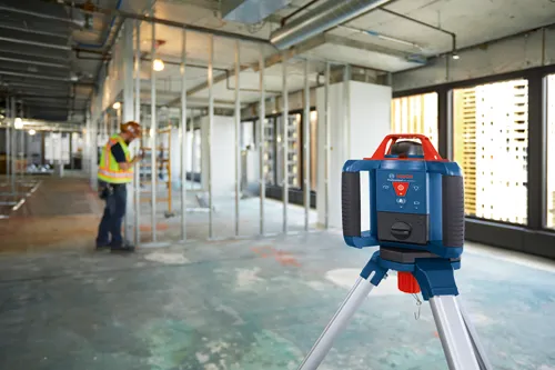Bosch GRL1000-20HV Láser Rotativo Profesional en una obra, con un trabajador que lleva casco y chaleco de seguridad en el fondo.