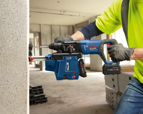 Bosch BULLDOG GBH18V-26D, taladro CORE18V, utilizado para taladrar en una pared de hormigón. Una persona con equipo de seguridad y guantes sujeta el taladro.