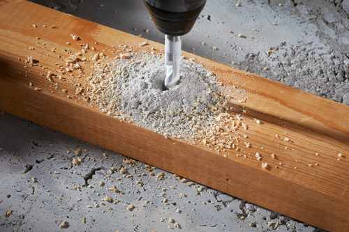 Broca perforando una tabla de madera, serrín alrededor del agujero.
