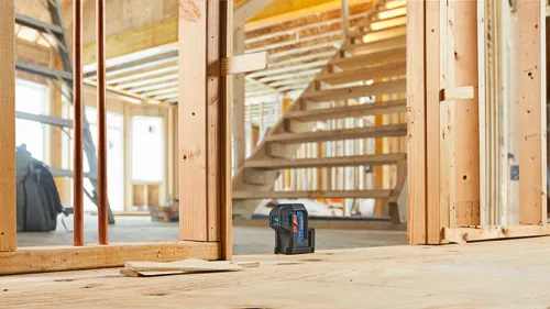 Nivel láser Bosch Professional en entorno de construcción, estructura de madera con una escalera al fondo.