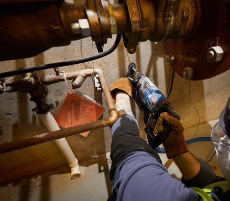 Persona con guantes utilizando un martillo perforador eléctrico Boschhammer de Bosch en tuberías de cobre.