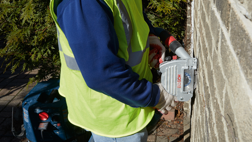 Persona con chaleco de seguridad utilizando una herramienta Bosch para cortar una pared de ladrillos.