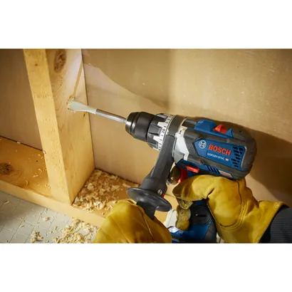 Bosch GSR18V-975C HD taladro en uso, con una broca insertada en una viga de madera, sostenida por una persona que lleva guantes.