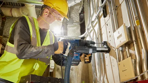 Persona con equipo de protección utilizando un martillo rotativo Boschhammer 1328VC para perforar una pared.