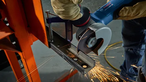 Amoladora angular Bosch GWS10-450P HD en uso, cortando una barra de metal, con chispas visibles.