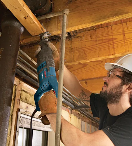 Persona que lleva gafas de seguridad y un casco utiliza una sierra recíproca para cortar una viga de madera.