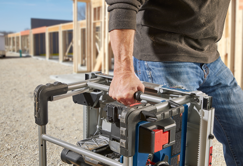 Persona sosteniendo una herramienta eléctrica Bosch, con una obra en construcción al fondo.