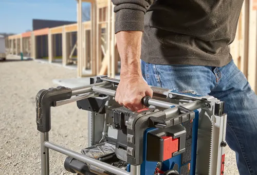 Persona sosteniendo una herramienta eléctrica Bosch, con una obra en construcción al fondo.