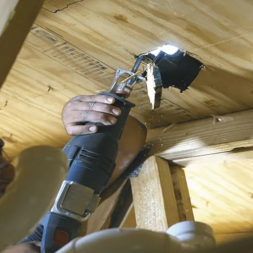 Persona utilizando una sierra sable para cortar un agujero en un techo de madera.