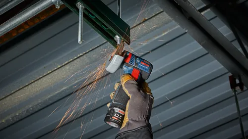 Amoladora angular Bosch GWS12V-30, emisión de chispas, sujeta por una mano enguantada con un paquete de baterías que indica "12 V 2.0 Ah Li-Ion".