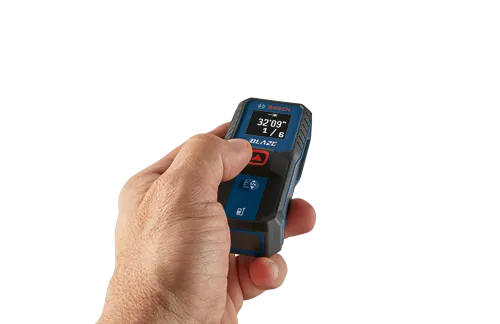 Una mano sostiene un medidor de distancia Bosch BLAZE, mostrando "32'09" 1/6".