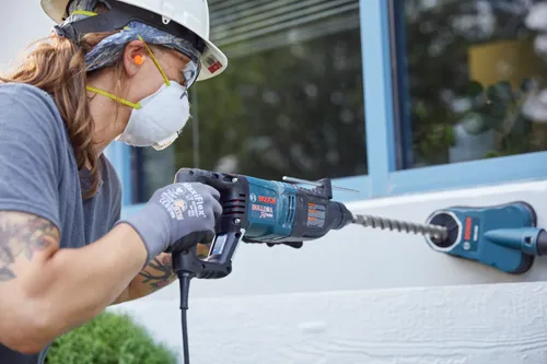 Persona utilizando un martillo rotativo Bosch BULLDOG Xtreme, con gafas de seguridad, tapones para los oídos y una mascarilla antipolvo.
