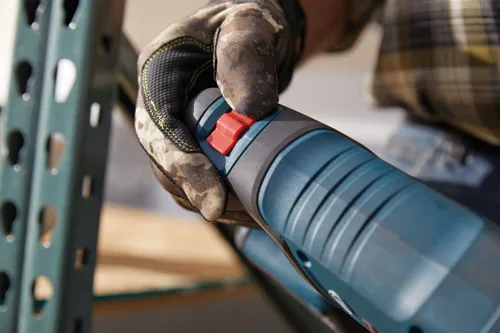 Una mano enguantada sosteniendo una herramienta eléctrica azul y negra con un botón rojo.