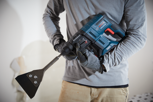 Taladro percutor rotativo Bosch GBH18V-21, con un accesorio de cincel, sostenido por una persona que lleva guantes de trabajo y una camisa gris de manga larga.