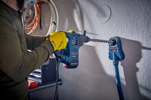 Persona que lleva equipo de protección utilizando un Boschhammer RH328VC de Bosch para perforar un agujero en una pared.