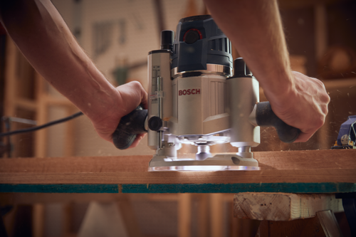 Manos sosteniendo una fresadora Bosch sobre una pieza de madera.
